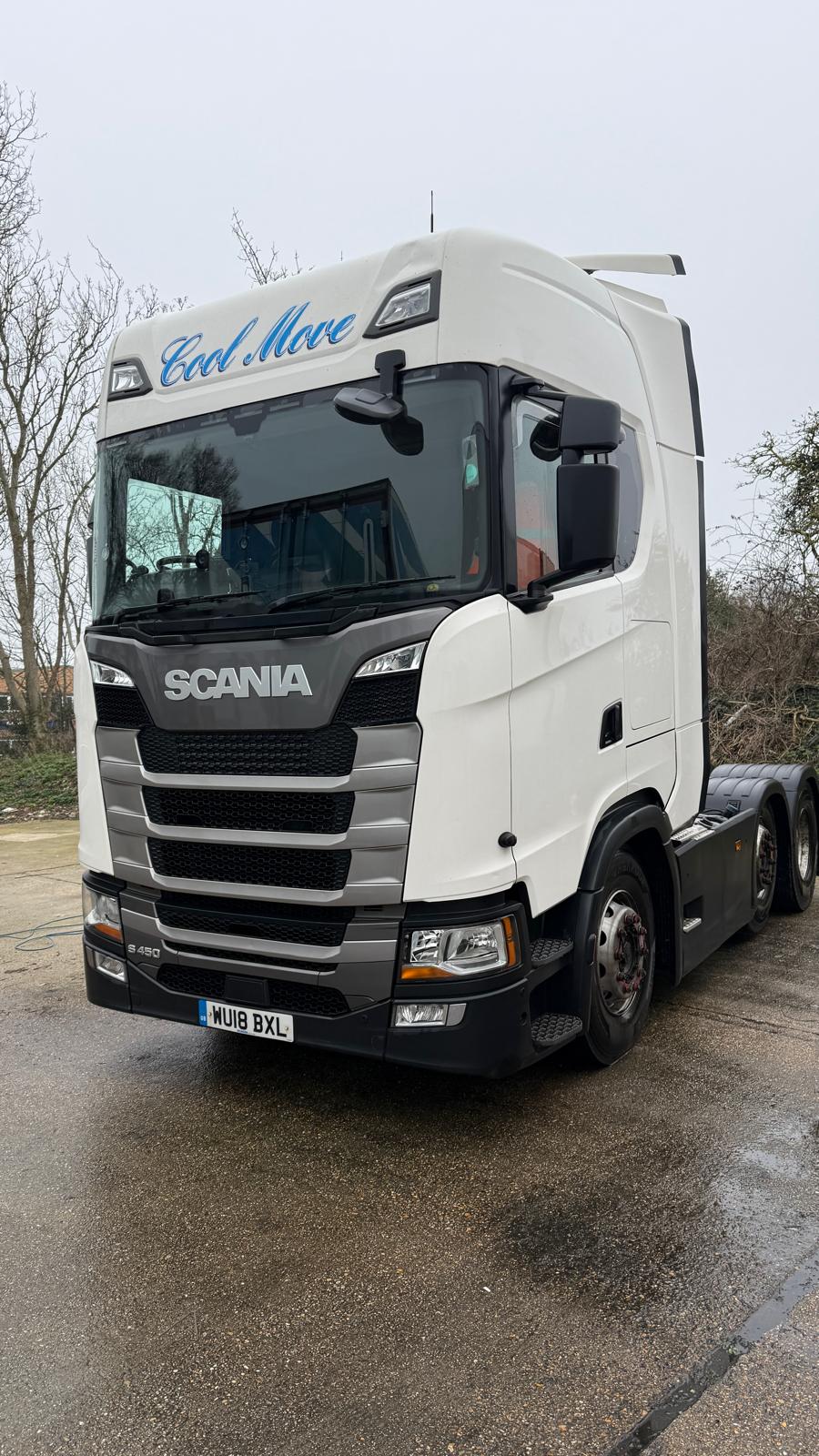 A white Cool Move Scania S450 tractor unit on a wet yard, photographed low at a three-quarter front angle.