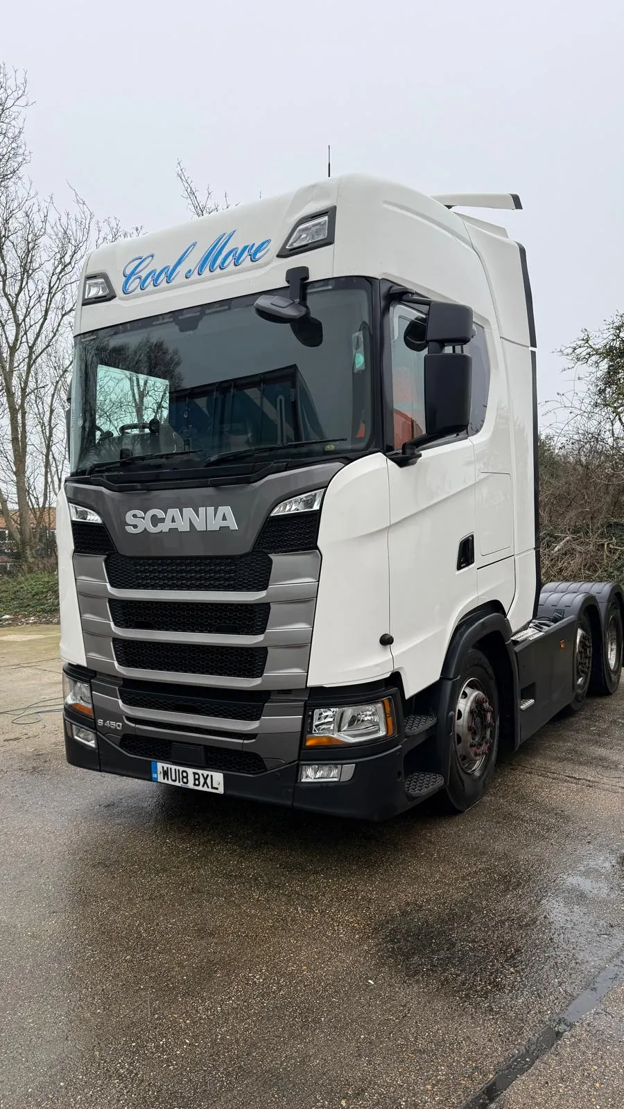 A white Cool Move Scania S450 tractor unit on a wet yard, low three-quarter front angle.